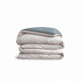 Down for Good Essential duvet cover panels, folded and stacked, in Shell and Blue Haze organic cotton.
